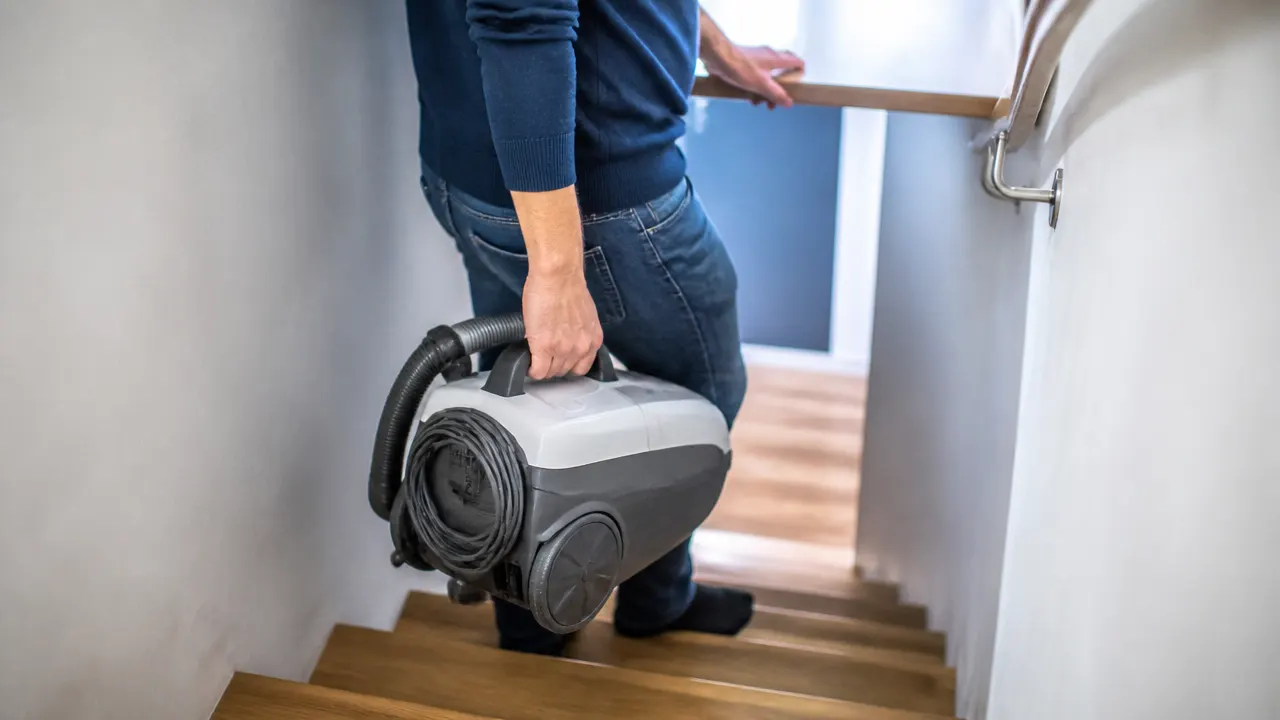 Utilisateur vu de dos portant un aspirateur traîneau dans un escalier